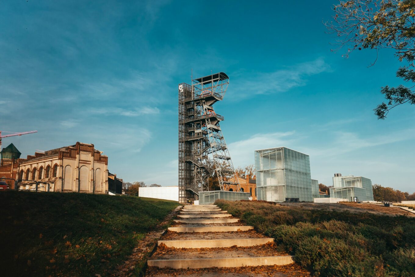 Nowoczesna wieża widokowa z metalu i szkła w Strefie Kultury w Katowicach, w otoczeniu postindustrialnych budynków i trawiastego wzniesienia.