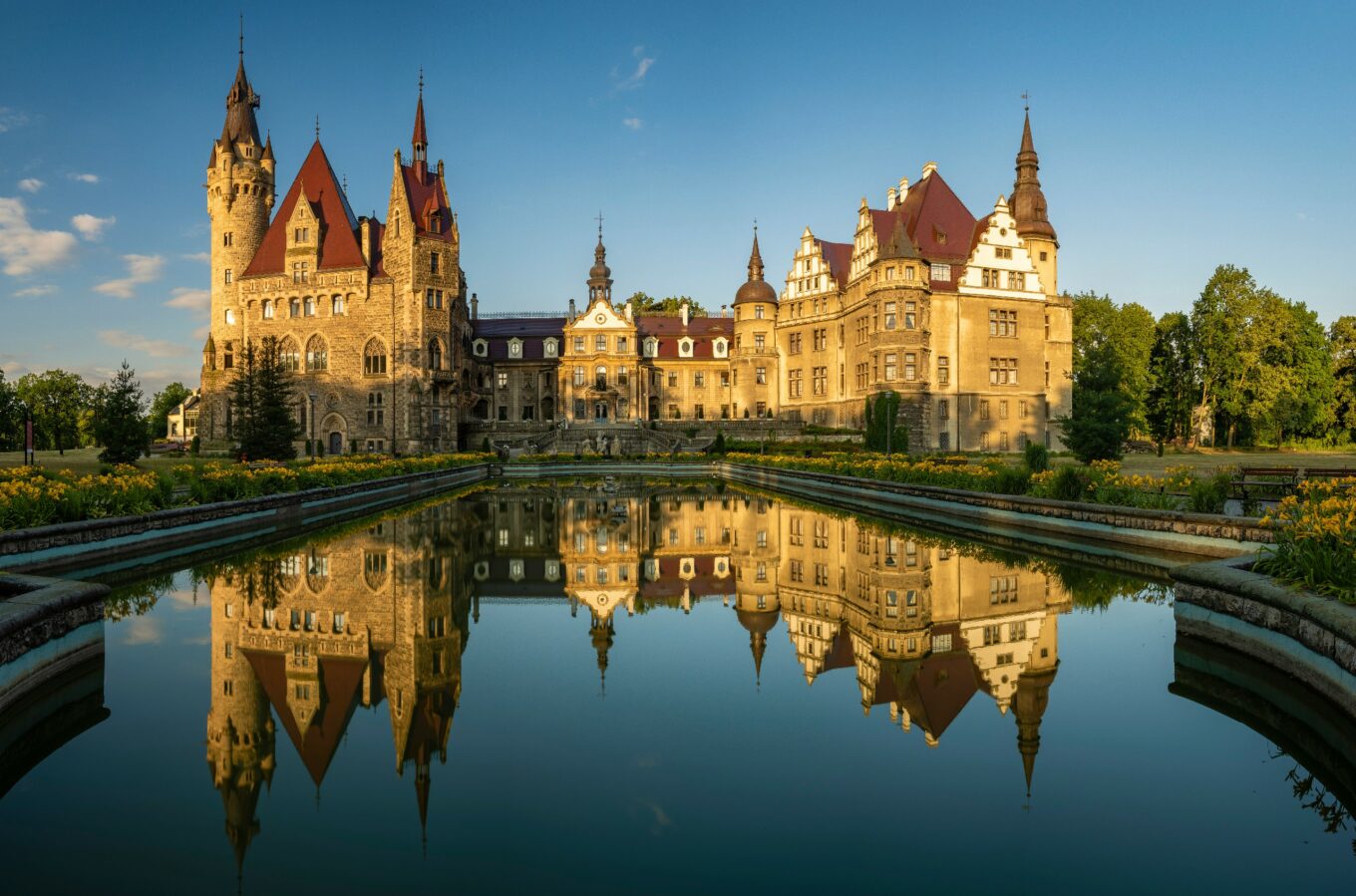 Widok na pałac z licznymi wieżami z odbiciem w stawie