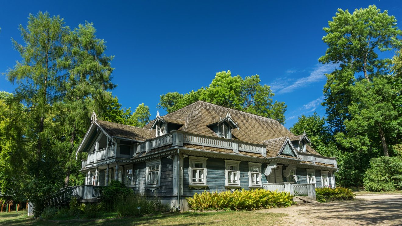 Zabytkowy drewniany budynek w stylu podlaskim otoczony drzewami