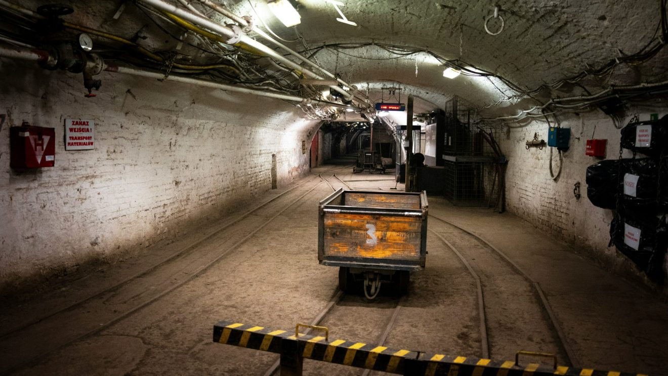 Podziemny tunel kopalni z torami, wózkiem transportowym i oświetleniem przemysłowym.